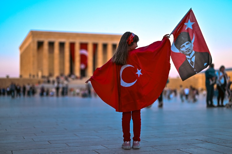 Sırtında Türk bayrağı ve elinde Atatürk ve Türk bayrağı olan çocuk