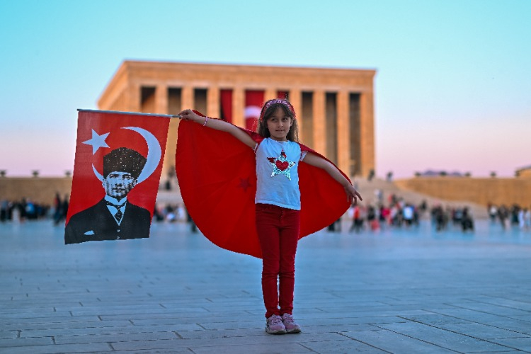 Sırtında Türk bayrağı ve elinde Atatürk ve Türk bayrağı olan çocuk